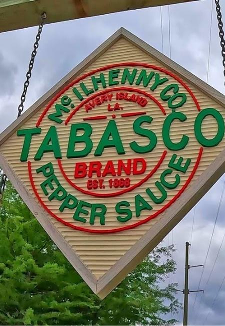 Das grün-rote Tabasco-Schild von McIlhenny Co. hängt auf Avery Island vor bewölktem Himmel und Stromleitungen.