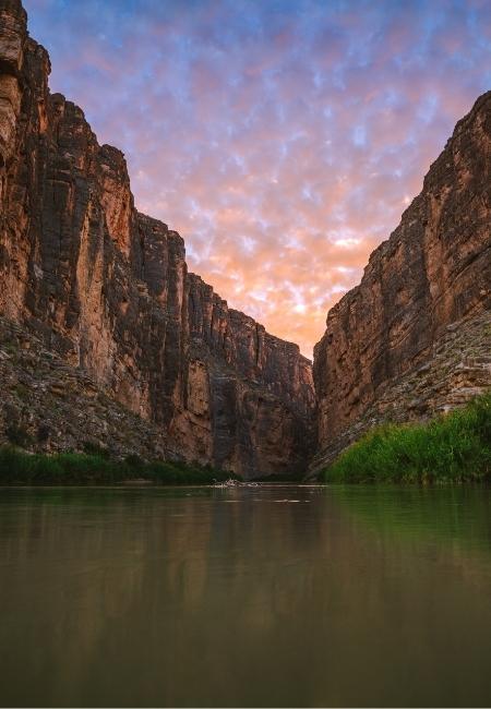 Im Big Bend National Park fließt ruhiges Wasser zwischen hohen Felswänden unter einem rosa Abendhimmel.