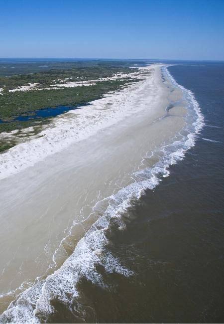 Eine lange helle Sandzunge von Cumberland Island National Seashore zieht sich zwischen Atlantik und Küstenvegetation entlang.