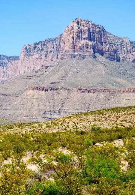 Vor den Guadalupe Mountains National Park erhebt sich eine steile Felswand über trockenem Buschland in Texas.