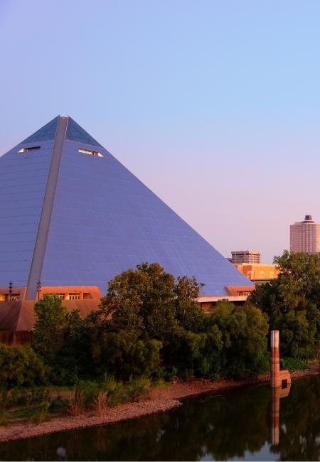 Die blau schimmernde Pyramide von Memphis erhebt sich über Bäumen und Wasser im warmen Abendlicht in Tennessee.