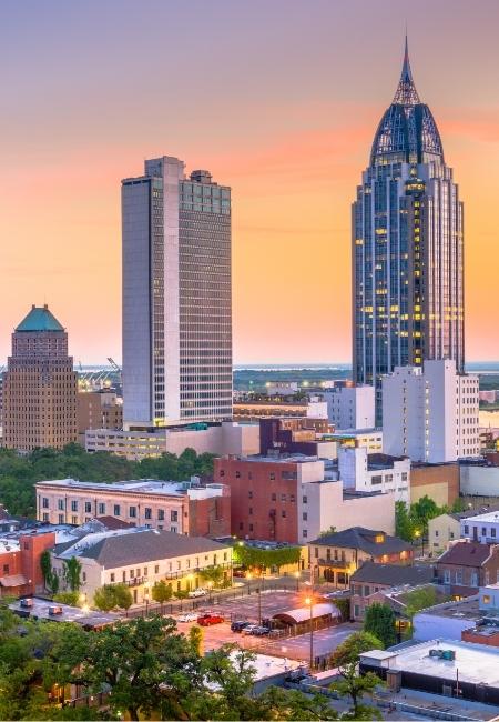 Die Skyline von Mobile, Alabama leuchtet im Abendlicht, während moderne Hochhäuser vor einem warmen Sonnenuntergang aufragen.