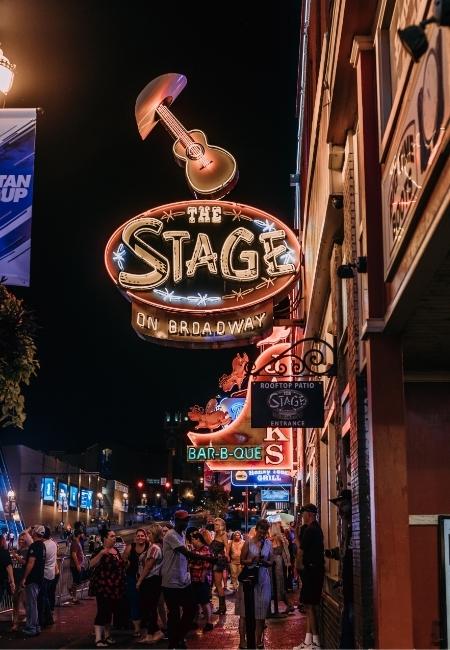 In der Nacht leuchtet The Stage an der Broadway Street in Nashville über einer belebten Straße mit vielen Passanten.
