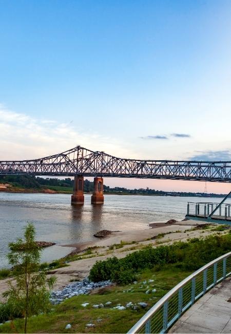 Die Stahlbrücke bei Natchez spannt sich über den Mississippi, während am Ufer ein ruhiger Spazierweg entlangführt.