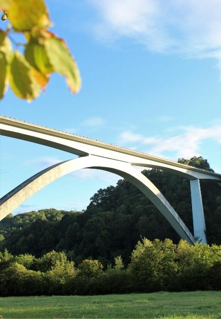 Das weiße Bogenviadukt der Natchez Trace Parkway spannt sich über bewaldete Hügel unter blauem Himmel.
