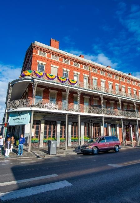 Ein historisches Backsteingebäude in New Orleans zeigt Monty’s Restaurant, davor stehen Autos und Passanten auf der Straße.