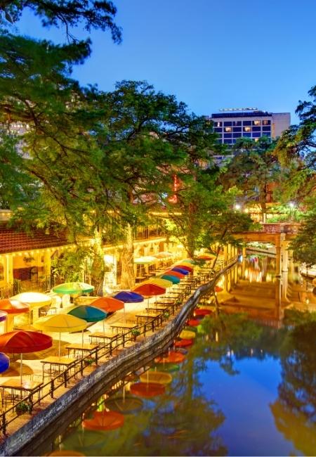 Am San-Antonio River Walk leuchten bunte Sonnenschirme entlang des Kanals, während sich die Lichter im Wasser spiegeln.