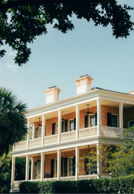 Ein weißes zweigeschossiges Südstaaten-Haus mit Veranda steht unter dichtem Baumgrün in Savannah, Georgia.