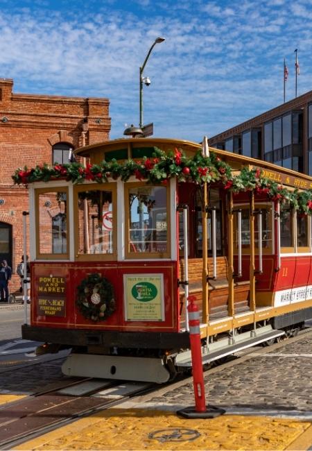 Das rot-gelbe Cable Car fährt an der Powell Street in San Francisco vorbei, festlich mit Tannengrün und Kränzen geschmückt.
