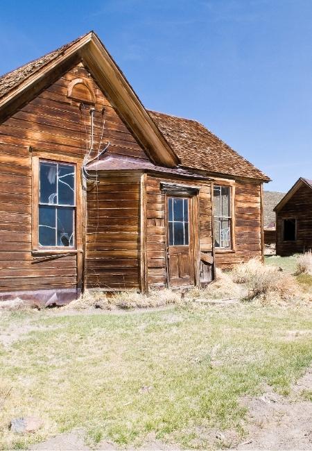 Ein verwittertes Holzhaus in der Geisterstadt Bodie steht zwischen trockenem Gras unter klarem Himmel.