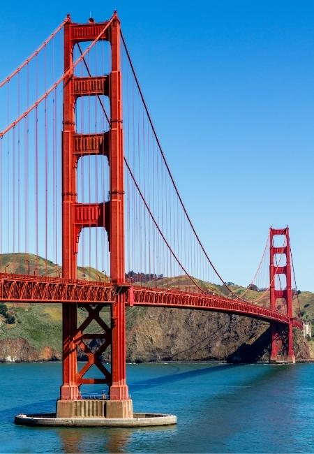 Die rote Golden Gate Bridge spannt sich über die Bucht von San Francisco, darunter leuchtet das blaue Wasser im Sonnenschein.