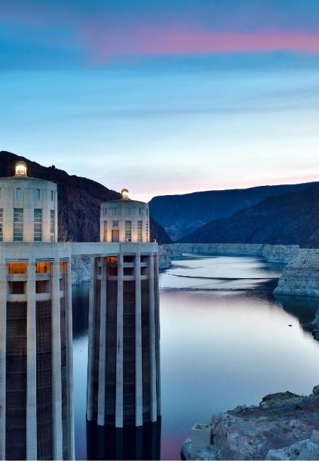 Das Hoover Dam ragt über das ruhige Wasser von Lake Mead, während der Himmel über den Bergen in Blau und Rosa leuchtet.