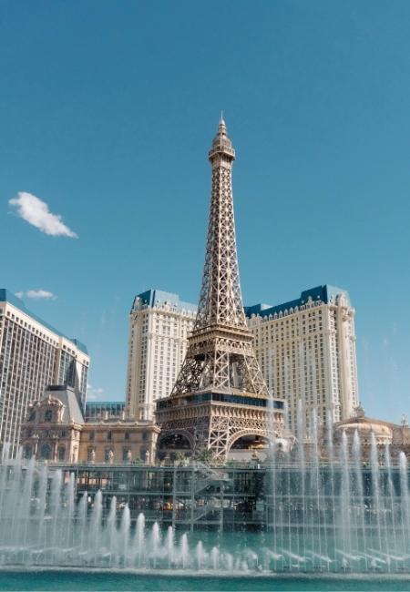 Der Eiffelturm von Paris Las Vegas ragt vor Hotelhochhäusern und Wasserfontänen unter klarem blauem Himmel auf.
