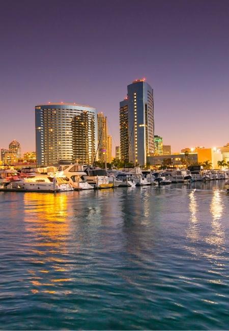 Die beleuchtete Skyline von San Diego spiegelt sich im ruhigen Wasser des Yachthafens, während Boote davor liegen.