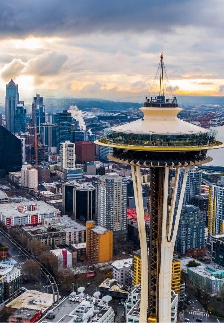 Die Space Needle ragt über die Skyline von Seattle, während am Horizont warmes Abendlicht unter dichten Wolken durchbricht.