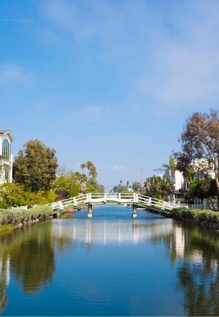 Die weiße Brücke über den Venice Canals in Los Angeles spiegelt sich ruhig im Wasser unter klarem Himmel.