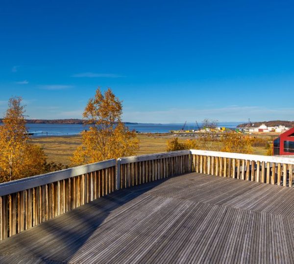 Eine weitläufige Holzterrasse mit goldenen Herbstbäumen, flachem Wasser und Gebäuden an der Küste von Anchorage in Alaska.