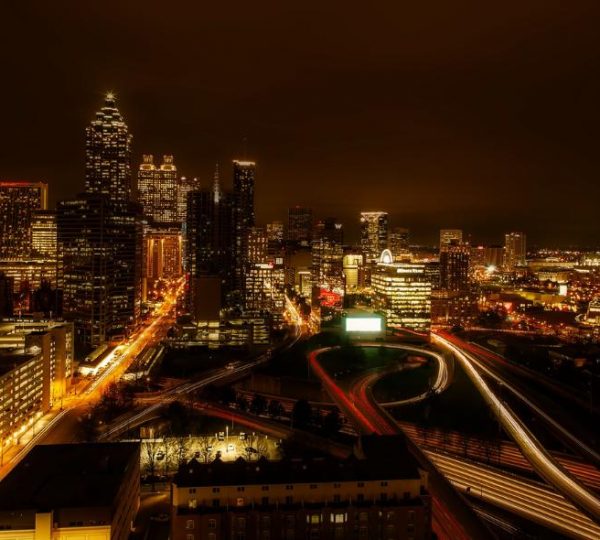 Beleuchtete Skyline von Atlanta bei Nacht mit Hochhäusern, dichten Schnellstraßen und langen Lichtspuren im Stadtverkehr.