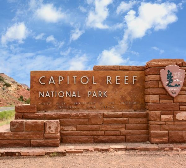 Ein rotes Sandsteinportal mit dem Schriftzug Capitol Reef National Park vor Felsen und blauem Himmel in Utah.