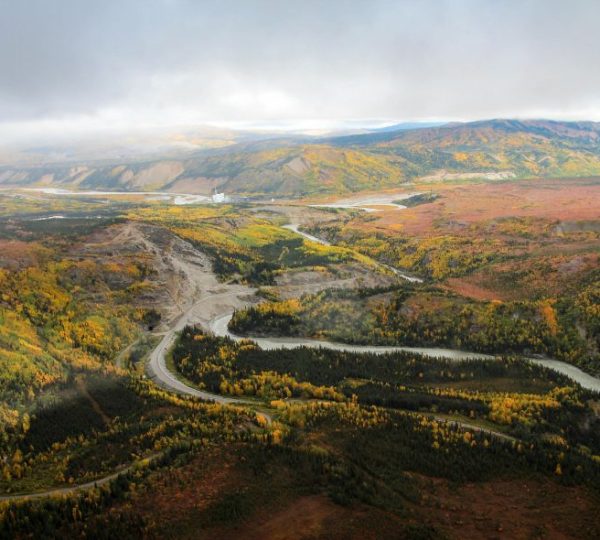 Weitläufige Herbstlandschaft im Denali Nationalpark mit gewundenem Fluss und bewaldeten Bergen nahe Anchorage in Alaska