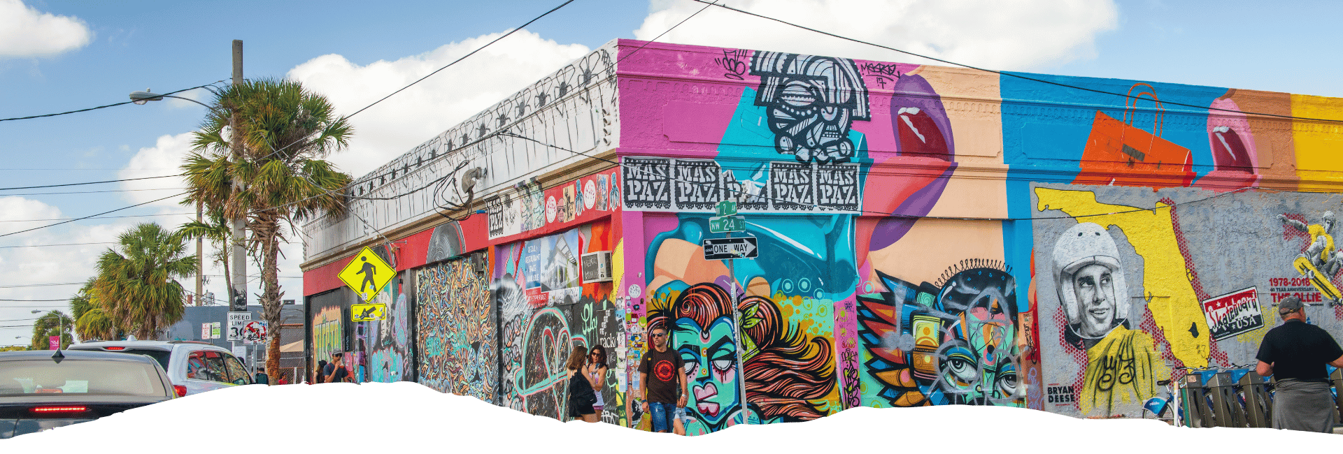 Bunte Street-Art-Fassade im Miami Design District mit Wandgemälden, Palmen und Passanten an einer belebten Straße