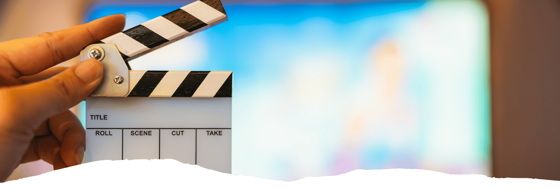 Eine geöffnete Filmklappe mit schwarz-weißen Streifen steht vor einer unscharfen Kulisse der Warner Bros Studios.