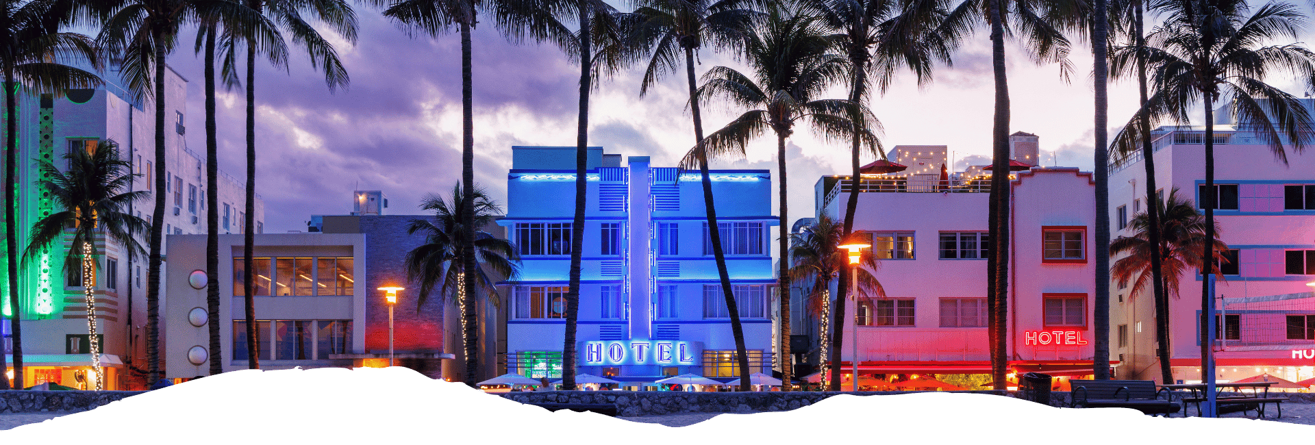 Bunte Art-déco-Hotels und hohe Palmen säumen den beleuchteten Ocean Drive in Miami Beach während der blauen Stunde.