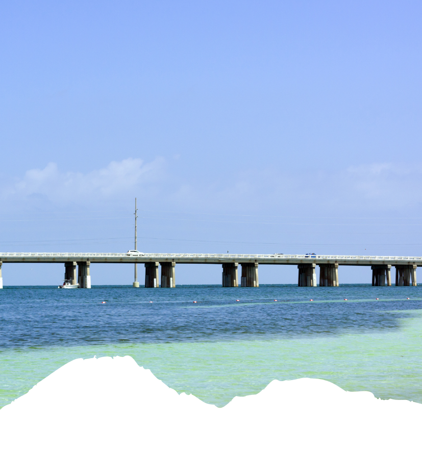 Eine lange Straßenbrücke führt über türkisfarbenes Wasser der Florida Keys; darunter ist eine dunkle Bergsilhouette zu sehen.