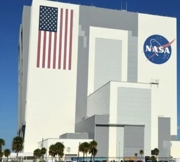 Das markante weiße NASA-Gebäude im Kennedy Space Center in Florida zeigt eine große US-Flagge und das NASA-Logo.