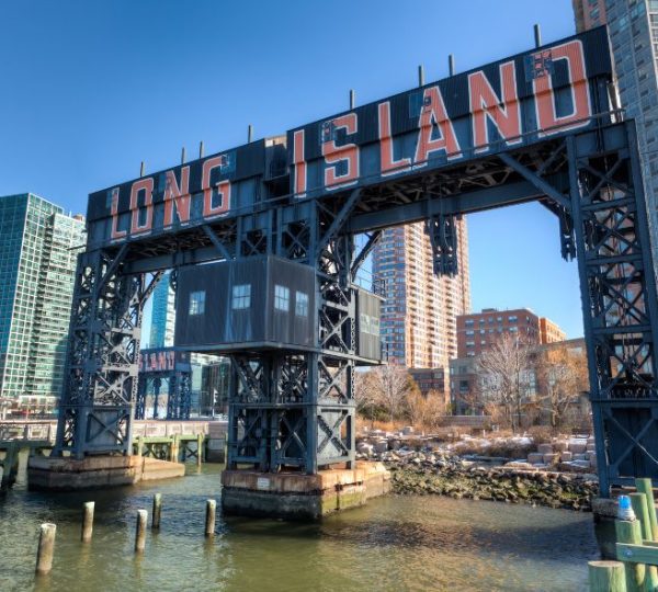 Ein markanter Long-Island-Schriftzug überspannt das Wasser zwischen Hochhäusern in New York bei winterlich klarem Wetter.