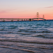 Wellen am Ufer des Michigansees vor der Mackinac Bridge bei rosa Abendhimmel während einer Michigan-Rundreise