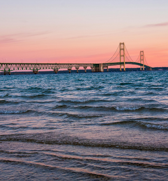 Wellen am Ufer des Michigansees vor der Mackinac Bridge bei rosa Abendhimmel während einer Michigan-Rundreise