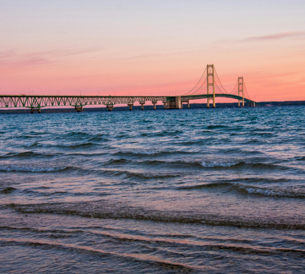 Wellen am Ufer des Michigansees vor der Mackinac Bridge bei rosa Abendhimmel während einer Michigan-Rundreise