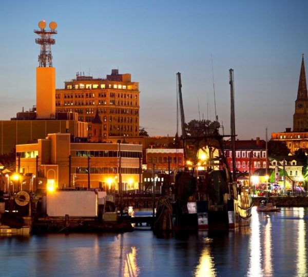 Abendlicher Hafen mit Segelschiff, beleuchteten Gebäuden und Kirchturm in New London während einer Neuenglandreise
