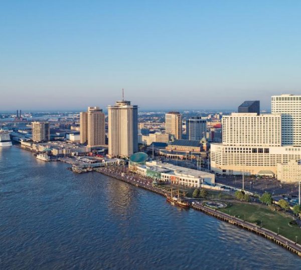 Luftaufnahme von New Orleans mit breitem Fluss, Hotels, Hochhäusern, Uferpromenade und einem Kreuzfahrtschiff