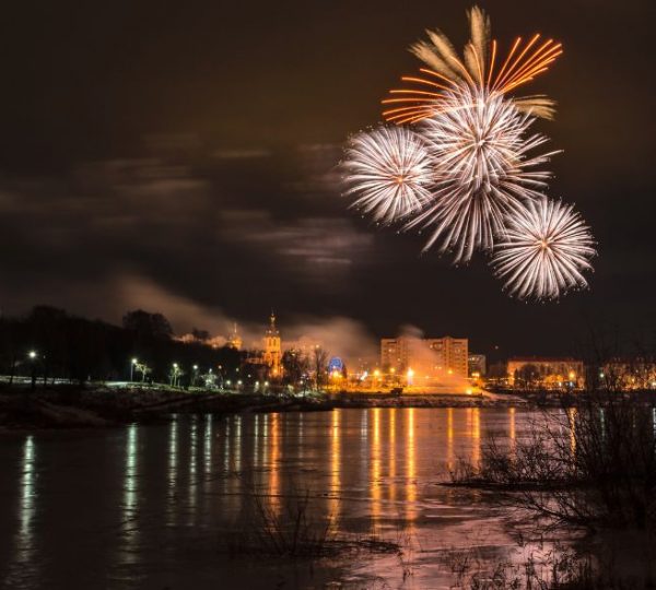 Nächtliches Feuerwerk über einer beleuchteten Uferkulisse in New York mit farbigen Spiegelungen auf dem Wasser