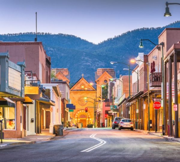 Belebte Geschäftsstraße in Santa Fe mit historischen Gebäuden, roten Felsen und bergiger Kulisse auf der Route 66