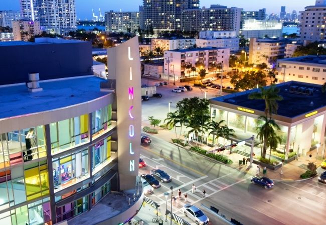 Beleuchtete Lincoln Road mit palmengesäumter Einkaufsmeile und Hochhäusern in Miami Beach bei beginnender Dunkelheit