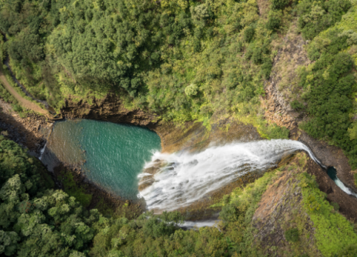 Türkisfarbenes Wasser sammelt sich unter einem breiten Wasserfall im üppig bewachsenen Volcano National Park auf Hawaii.