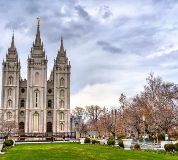 Im Stadtpark von Salt Lake City steht der hohe Salt Lake Temple mit drei Türmen vor einem bewölkten Himmel und kahlen Bäumen.