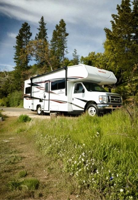 Ein mittleres Wohnmobil steht auf einem Waldweg zwischen hohen Bäumen und zeigt die Wohnmobilklasse für Reisen in den USA.