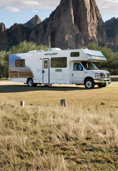 Ein großes Class-C-Wohnmobil steht auf einer Wiese vor steilen Felsformationen und erinnert an eine USA-Rundreise.