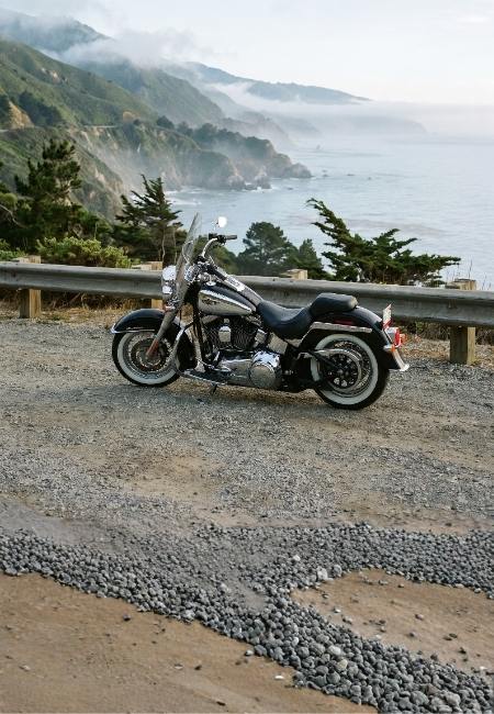 Ein schwarzes Cruiser-Motorrad steht an einer Küstenstraße vor nebligen Klippen und dem ruhigen Meer.