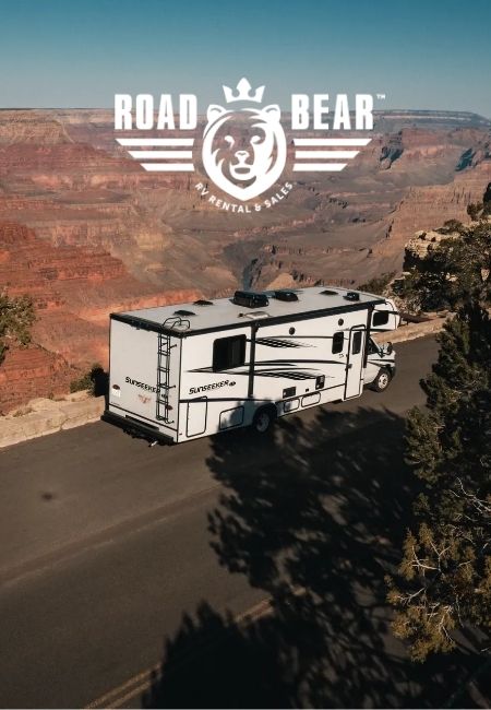 Ein weißes Road Bear RV fährt auf einer kurvigen Straße am Rand eines roten Canyon-Massivs entlang.