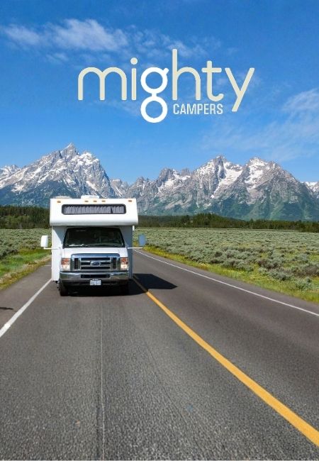 Ein weißes Mighty-Campers-Wohnmobil fährt auf einer Asphaltstraße vor schneebedeckten Bergen und blauem Himmel.