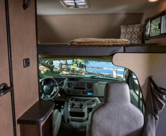 Blick in ein Cruise America Wohnmobil mit Fahrerhaus, Alkovenbett über der Kabine und kompakter Wohnkabine.