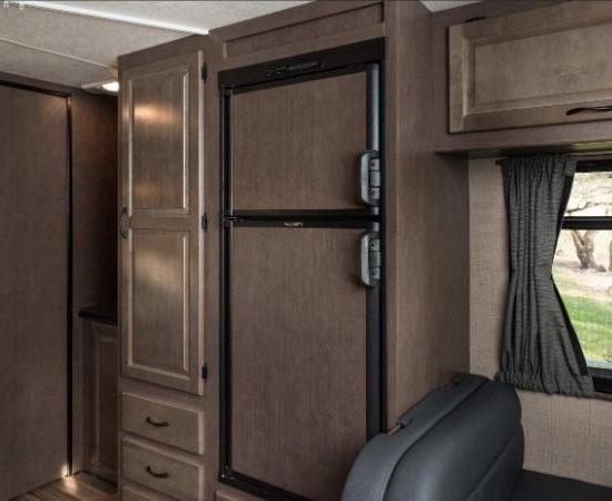 Im Wohnmobil von Cruise America sind ein Kühlschrank, braune Schränke und ein Fenster mit Blick ins Grüne zu sehen.