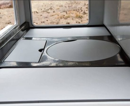 Im Wohnmobil ist eine graue Küchenarbeitsfläche mit runder Spülenabdeckung und Blick durch das Fenster auf die Wüste zu sehen.
