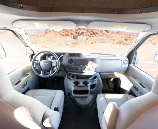 Im Cockpit des Road Bear Class C stehen zwei helle Sitze vor Armaturenbrett und Windschutzscheibe mit Wüstenlandschaft.