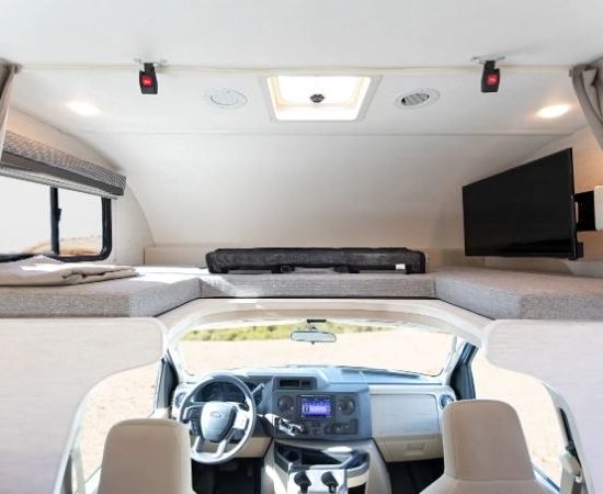 Heller Innenraum eines Road Bear Class C mit Alkovenbett, Fernseher, Küchenbereich und integriertem Fahrerhaus